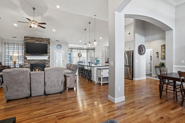 living room with a fireplace, light hardwood / wood-style floors, high vaulted ceiling, and ceiling fan