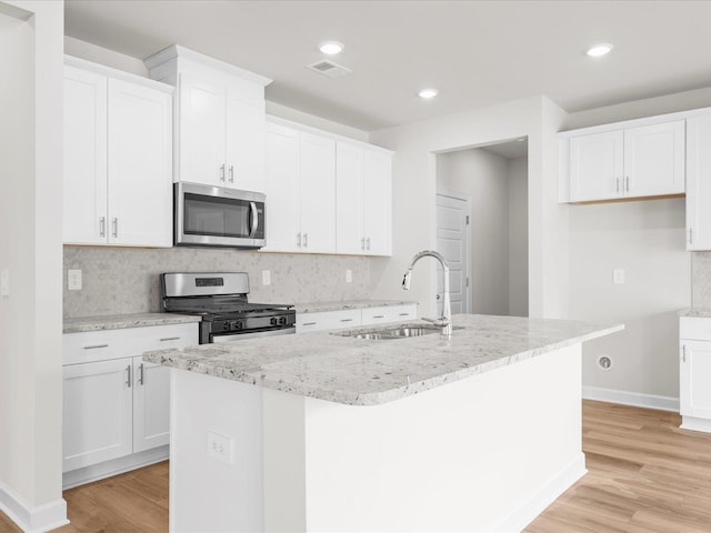 kitchen with appliances with stainless steel finishes, a kitchen island with sink, sink, and white cabinets