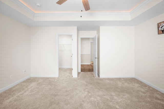 unfurnished bedroom featuring a walk in closet, light colored carpet, a raised ceiling, and ceiling fan