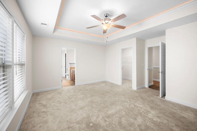 unfurnished bedroom with ceiling fan, a spacious closet, light carpet, and a tray ceiling