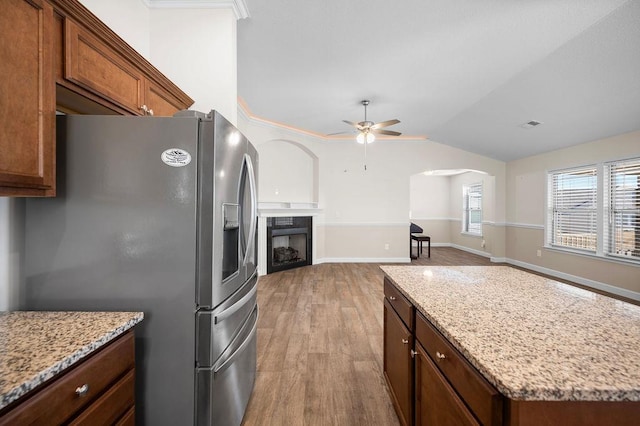 kitchen featuring ceiling fan, a center island, light stone countertops, stainless steel fridge, and light wood-type flooring