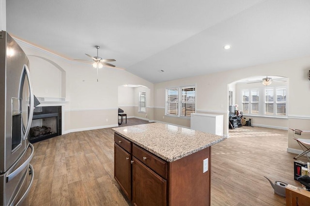 kitchen featuring a center island, vaulted ceiling, stainless steel fridge, light wood-type flooring, and light stone counters