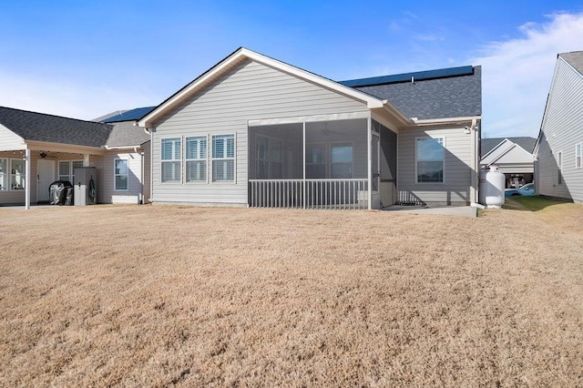 rear view of house with a sunroom, solar panels, and a lawn