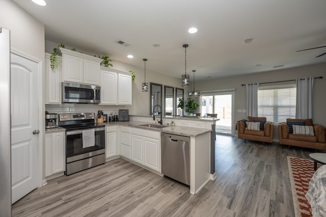 kitchen with kitchen peninsula, stainless steel appliances, sink, pendant lighting, and white cabinetry