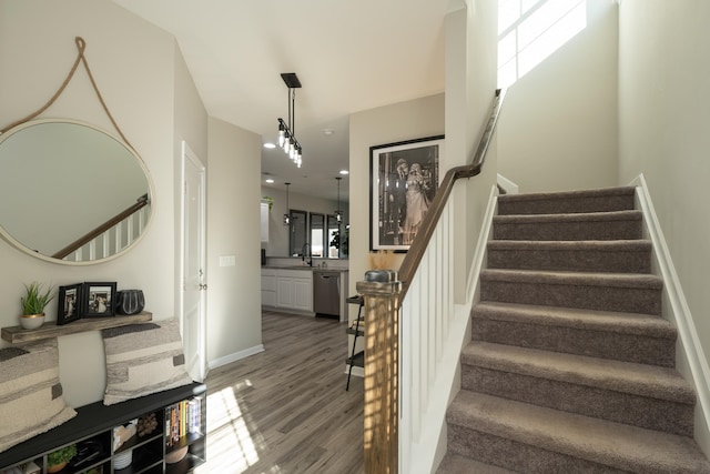 stairway featuring a healthy amount of sunlight, wood-type flooring, sink, and an inviting chandelier