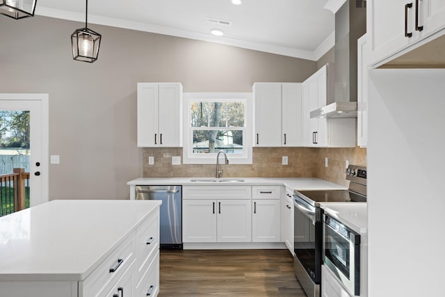 kitchen with wall chimney exhaust hood, stainless steel appliances, sink, white cabinetry, and hanging light fixtures