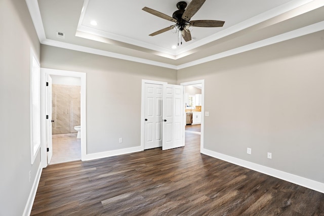 unfurnished bedroom with dark wood-type flooring, crown molding, ceiling fan, connected bathroom, and a tray ceiling