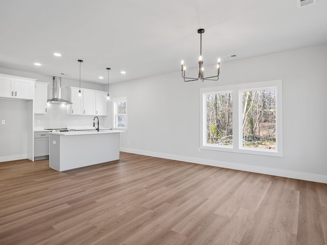 kitchen with a kitchen island with sink, wall chimney range hood, pendant lighting, light hardwood / wood-style flooring, and white cabinetry