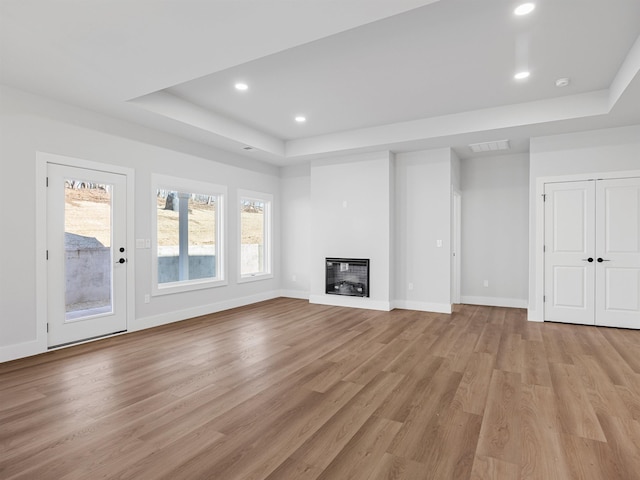 unfurnished living room with a raised ceiling, light hardwood / wood-style flooring, and plenty of natural light