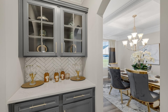 bar featuring backsplash, hanging light fixtures, hardwood / wood-style flooring, light stone countertops, and a notable chandelier