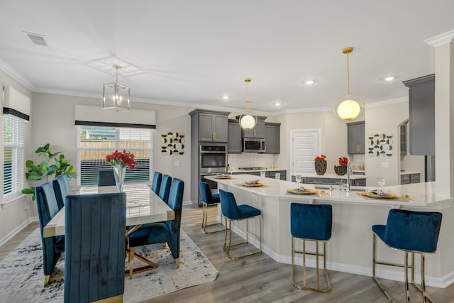 kitchen with stainless steel appliances, hardwood / wood-style floors, gray cabinets, hanging light fixtures, and a breakfast bar area