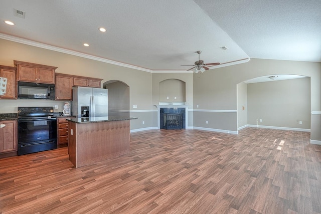 kitchen with ceiling fan, dark wood-type flooring, black appliances, a center island, and a tiled fireplace