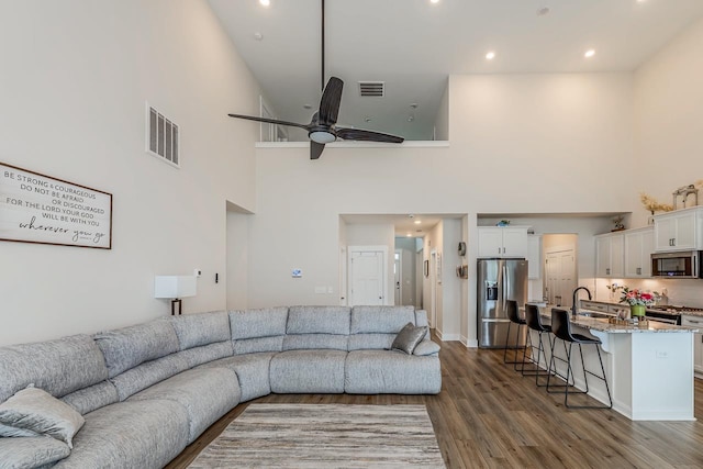 living room with a towering ceiling, hardwood / wood-style flooring, ceiling fan, and sink