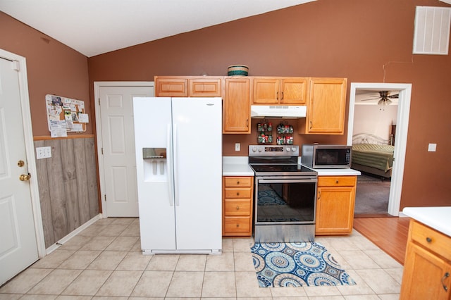 kitchen featuring ceiling fan, lofted ceiling, wooden walls, light tile patterned floors, and appliances with stainless steel finishes