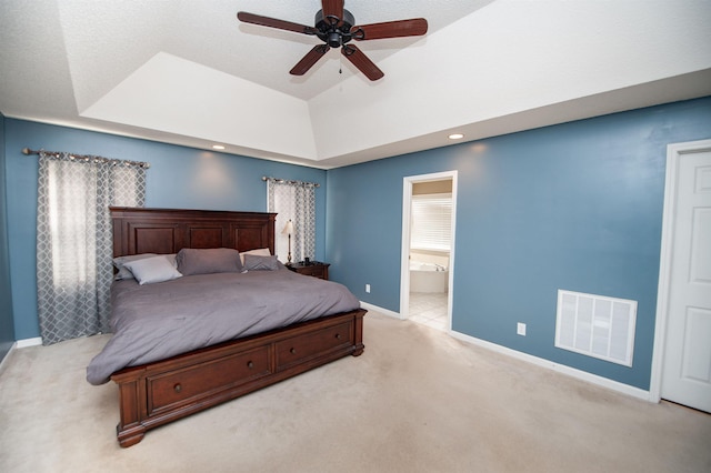 bedroom with ceiling fan, a raised ceiling, light carpet, and connected bathroom