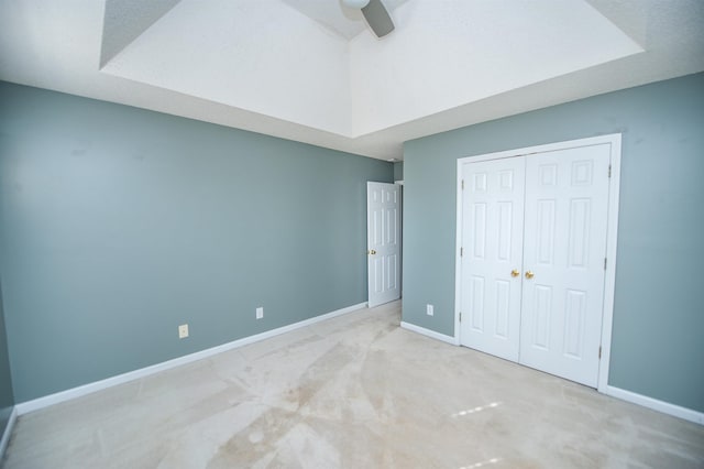 unfurnished bedroom featuring a closet, ceiling fan, light colored carpet, and a tray ceiling