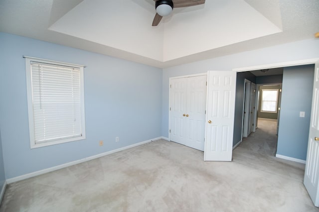 unfurnished bedroom with a raised ceiling, ceiling fan, light colored carpet, and a closet