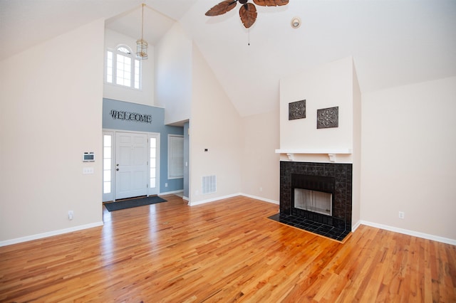 unfurnished living room featuring a tile fireplace, high vaulted ceiling, ceiling fan with notable chandelier, and hardwood / wood-style flooring