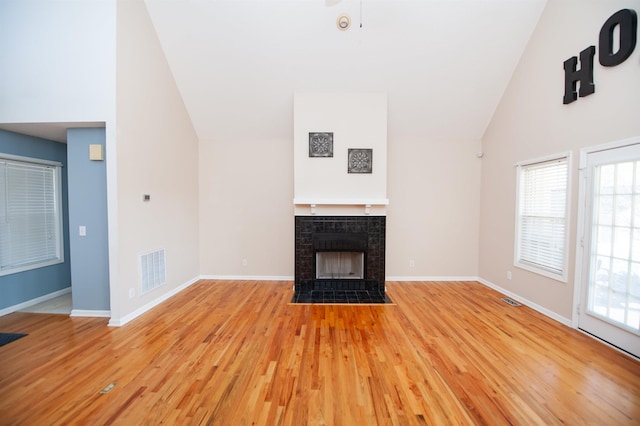 unfurnished living room featuring high vaulted ceiling, a tile fireplace, and light hardwood / wood-style flooring