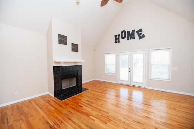 unfurnished living room featuring ceiling fan, french doors, high vaulted ceiling, hardwood / wood-style floors, and a tiled fireplace