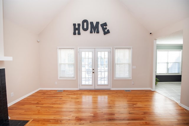 unfurnished living room featuring light hardwood / wood-style floors, a tiled fireplace, high vaulted ceiling, and french doors