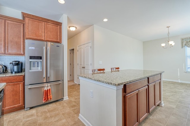 kitchen featuring stainless steel refrigerator with ice dispenser, pendant lighting, light stone counters, and a notable chandelier