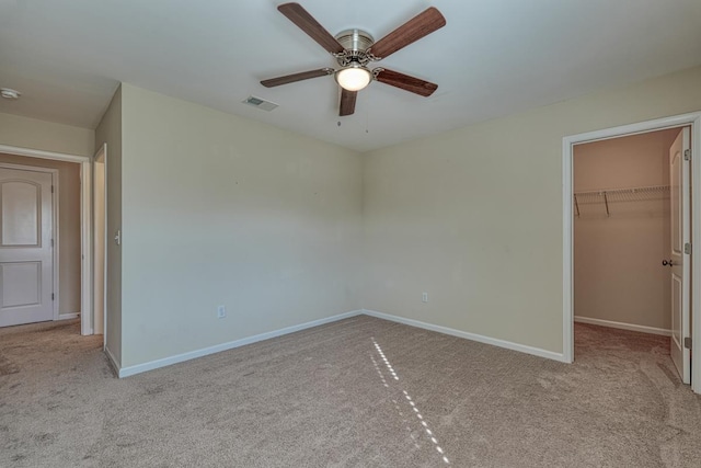 unfurnished bedroom featuring a spacious closet, a closet, ceiling fan, and light colored carpet