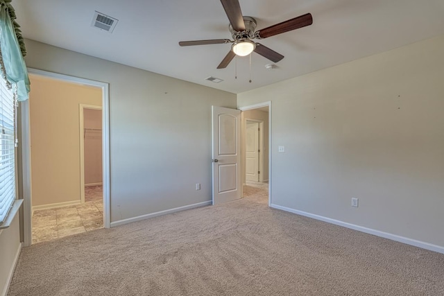 unfurnished bedroom featuring a walk in closet, ceiling fan, a closet, and light carpet