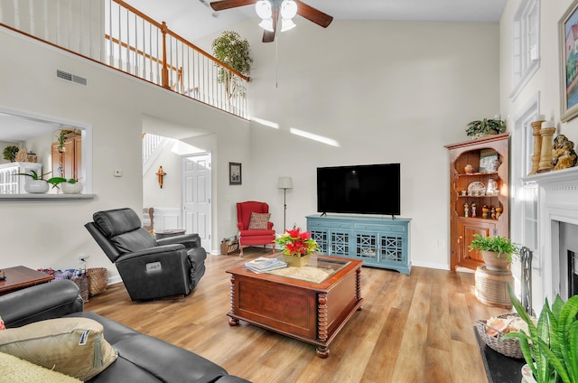 living room featuring ceiling fan, light hardwood / wood-style floors, and a towering ceiling