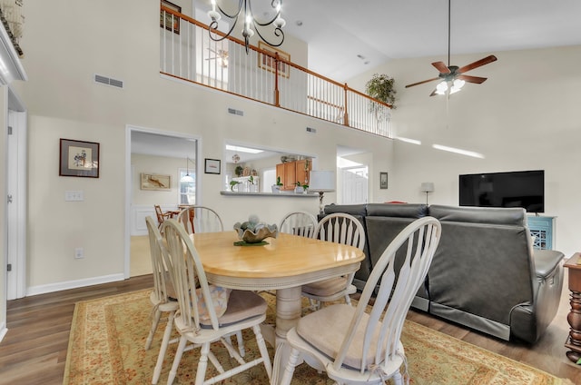 dining space with hardwood / wood-style floors, ceiling fan with notable chandelier, and high vaulted ceiling