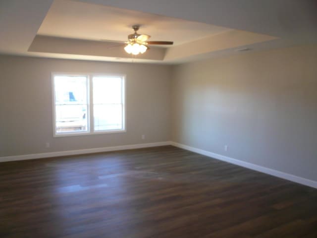 spare room with a tray ceiling, ceiling fan, and dark wood-type flooring