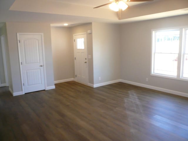 foyer with a raised ceiling, ceiling fan, and dark wood-type flooring