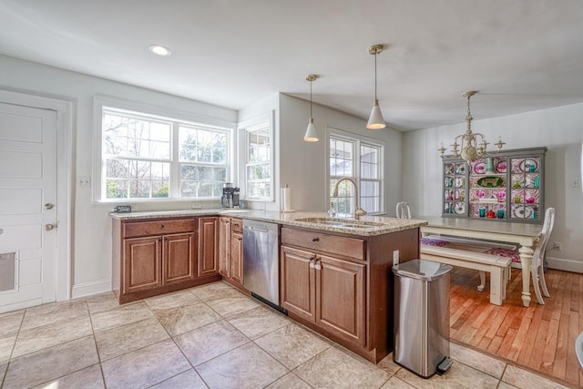 kitchen with light stone counters, stainless steel dishwasher, sink, light tile patterned floors, and hanging light fixtures