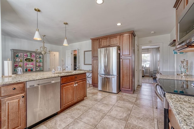 kitchen with decorative light fixtures, sink, light stone counters, and stainless steel appliances