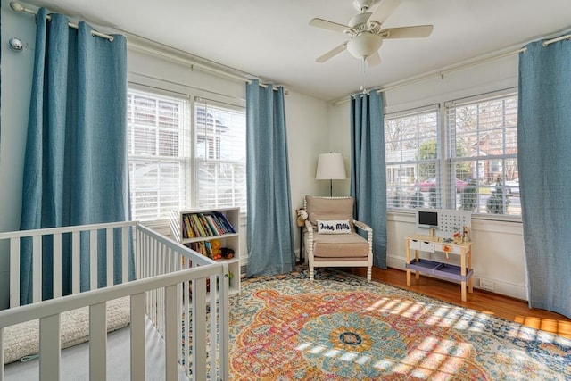 bedroom featuring multiple windows, ceiling fan, a nursery area, and hardwood / wood-style flooring