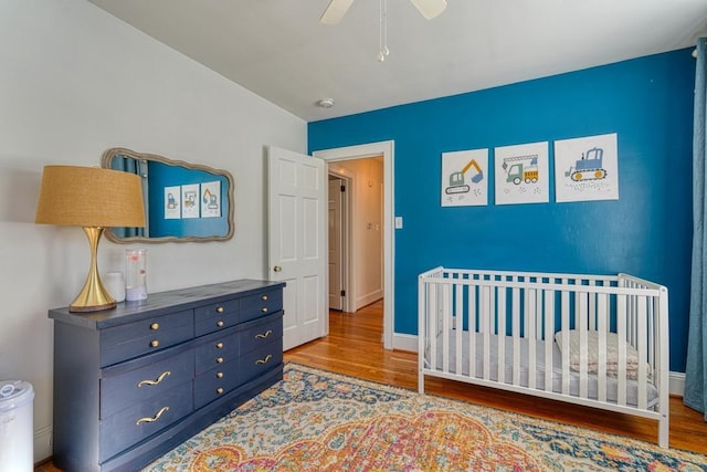 bedroom featuring hardwood / wood-style flooring, ceiling fan, and a crib