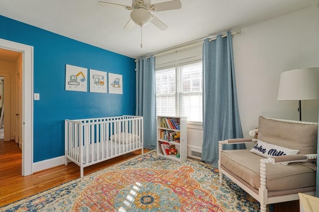 bedroom with hardwood / wood-style floors, ceiling fan, and a crib