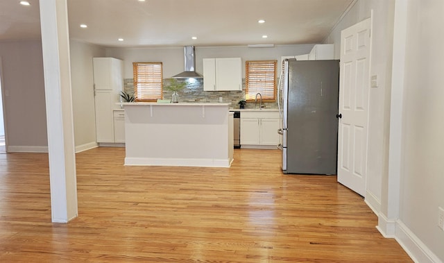 kitchen with backsplash, wall chimney exhaust hood, appliances with stainless steel finishes, a kitchen island, and white cabinetry