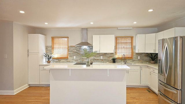 kitchen featuring sink, wall chimney exhaust hood, a kitchen island, stainless steel fridge with ice dispenser, and white cabinets