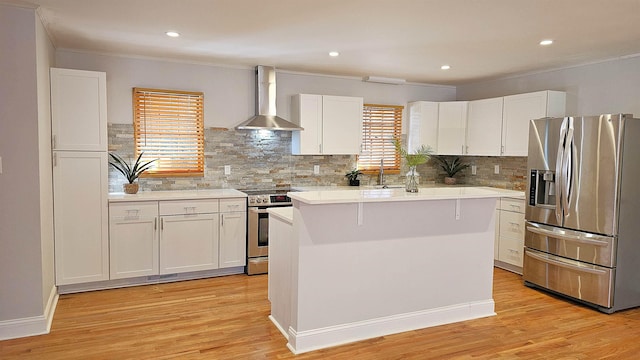 kitchen featuring wall chimney range hood, a kitchen island, backsplash, white cabinets, and appliances with stainless steel finishes