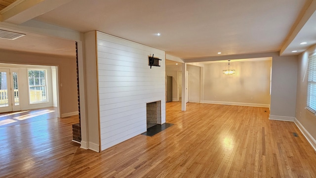 unfurnished living room featuring a large fireplace, light hardwood / wood-style flooring, and an inviting chandelier