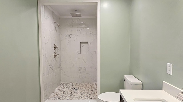 bathroom with toilet, vanity, ornamental molding, and tiled shower