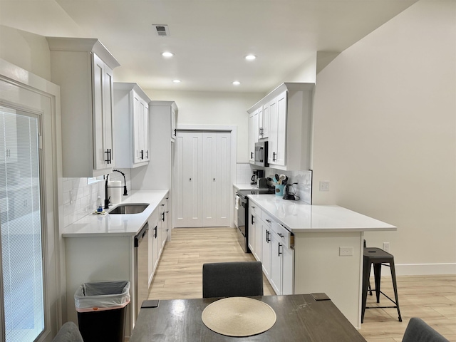 kitchen with a breakfast bar, white cabinets, sink, decorative backsplash, and stainless steel appliances