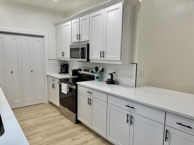 kitchen with light wood-type flooring, white cabinetry, appliances with stainless steel finishes, and tasteful backsplash