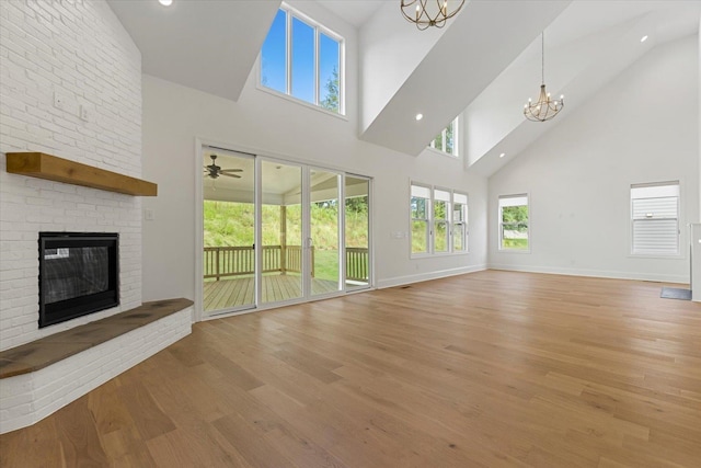 unfurnished living room with a brick fireplace, light hardwood / wood-style flooring, a high ceiling, and a notable chandelier