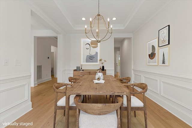 dining room featuring a raised ceiling, light wood-type flooring, crown molding, and a chandelier