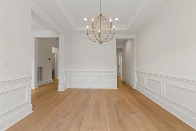 unfurnished dining area with ornamental molding, light wood-type flooring, a tray ceiling, and a notable chandelier