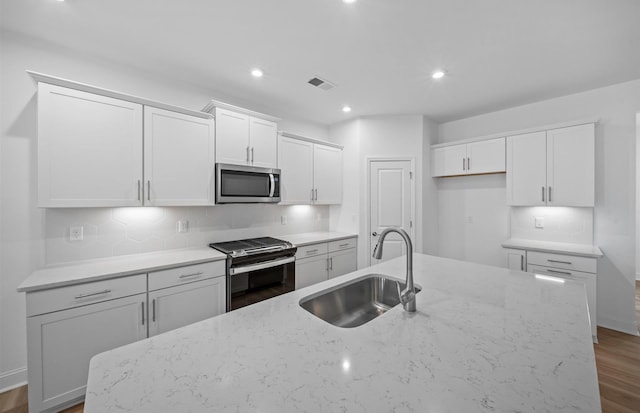 kitchen with a kitchen island with sink, white cabinets, sink, light stone countertops, and appliances with stainless steel finishes