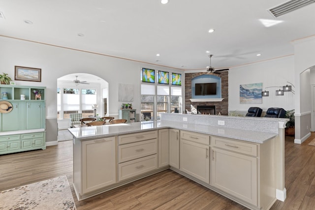 kitchen featuring cream cabinets, a stone fireplace, crown molding, light stone countertops, and light hardwood / wood-style floors