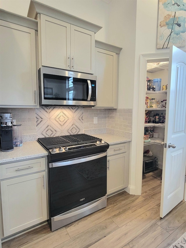 kitchen featuring stainless steel appliances, tasteful backsplash, light stone counters, light hardwood / wood-style flooring, and gray cabinets